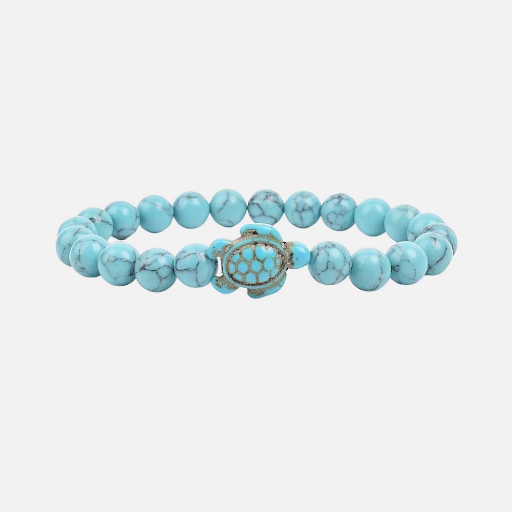 Ce bracelet de perles, orné d'une tortue délicate, brille comme un trésor rare trouvé dans les profondeurs des océans, prêt à enchanter celui qui le porte