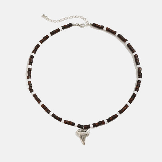 Ce collier en perles marron et blanches, orné d'un pendentif en forme de dent de requin, évoque l'âme aventureuse des marins des temps anciens
