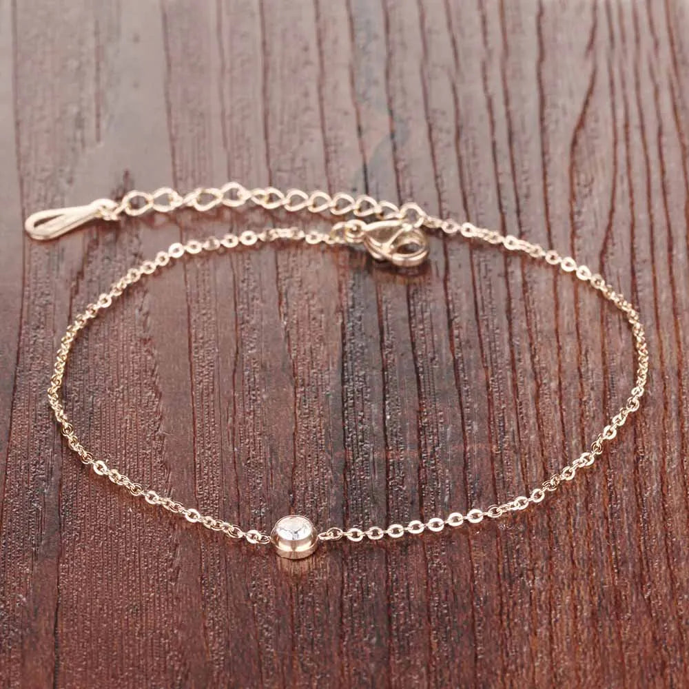 Comme une goutte d'or pure, ce bracelet fin enlace la cheville avec la douceur d'une vague au coucher du soleil, portant en son cœur une gemme scintillante comme l'étoile du matin sur la mer calme