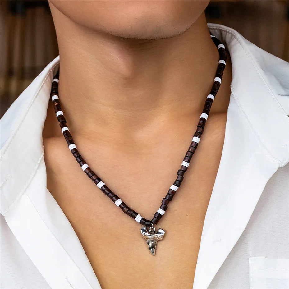 Ce collier en perles marron et blanches, orné d'un pendentif en forme de dent de requin, évoque l'âme aventureuse des marins des temps anciens