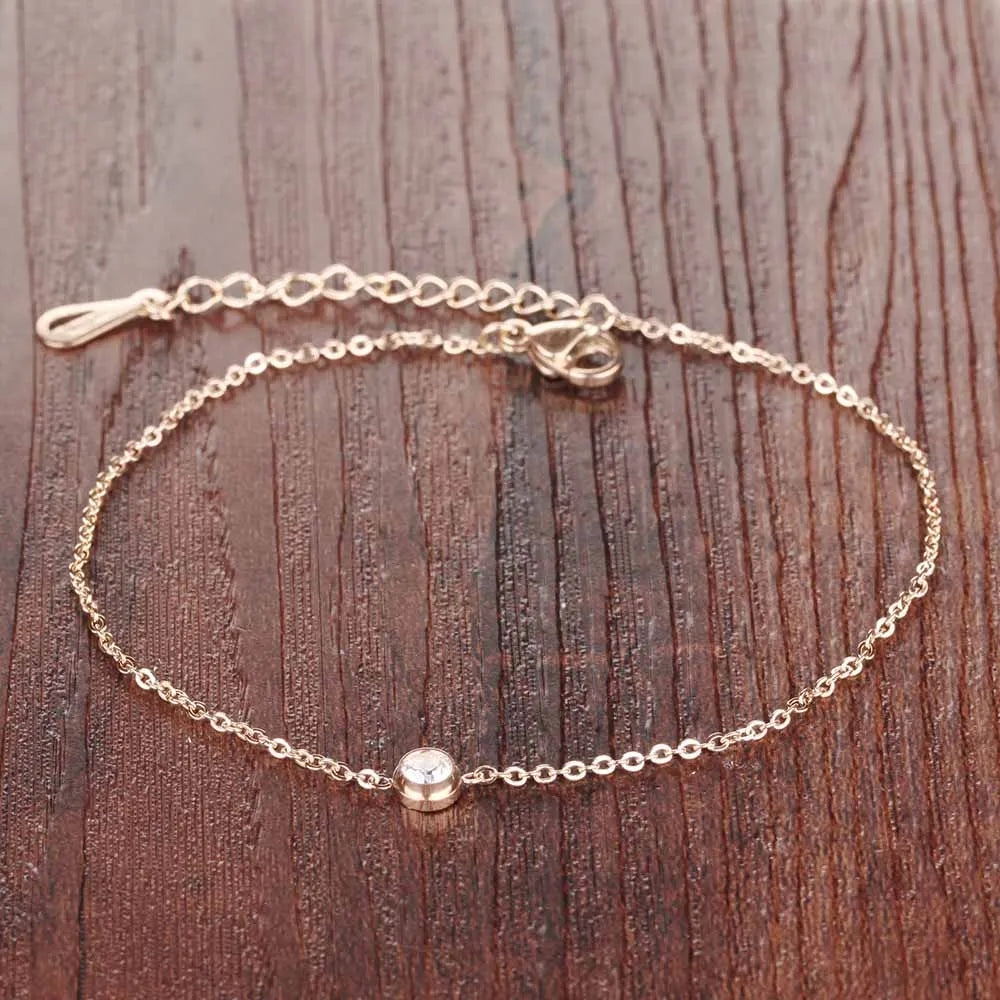 Comme une goutte d'or pure, ce bracelet fin enlace la cheville avec la douceur d'une vague au coucher du soleil, portant en son cœur une gemme scintillante comme l'étoile du matin sur la mer calme
